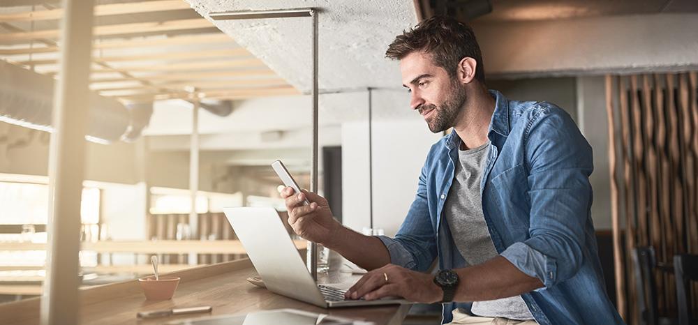 Man Using Laptop At Bench also look at mobile phone